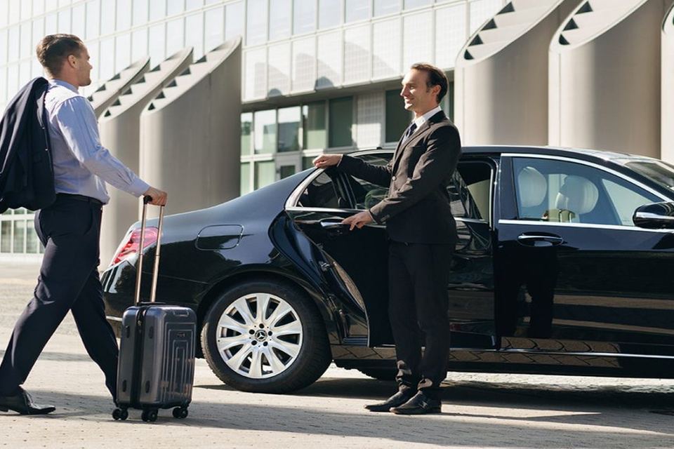 Geschäftsreisender mit Koffer, der Chauffeur öffnet die Tür der Limousine