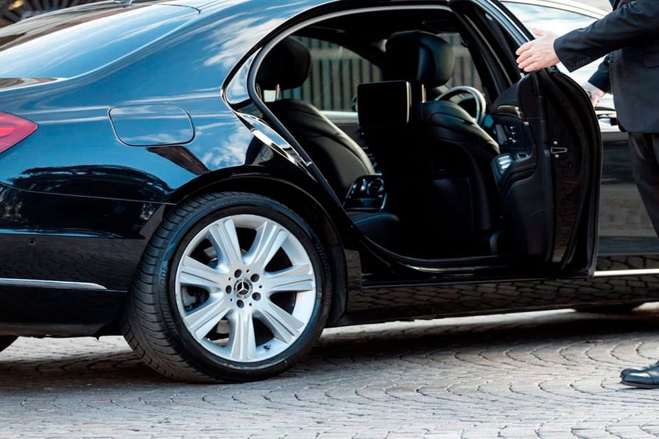 Offene hintere Tür einer schwarzen Limousine, der Chauffeur hält sie auf